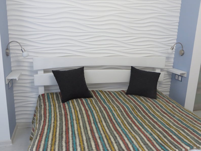 Puede incluir: Una estructura de cama blanca con una cabecera con un patr&oacute;n de ondas. La cama tiene una manta a rayas y dos almohadas negras. Hay dos apliques de pared con bombillas a cada lado de la cama.