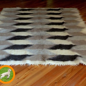 Puede incluir: Una alfombra de lana blanca, gris y negra con un patrón geométrico de diamantes. La alfombra tiene una textura peluda y está hecha de fibras naturales.