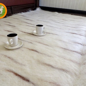 Puede incluir: Dos tazas de café blancas con platillos sobre una alfombra blanca y esponjosa con rayas marrones.