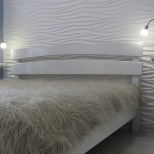 May include: A white bed frame with a fluffy white and gray blanket. The headboard is curved and has a modern design. The wall behind the bed is white with a textured pattern.
