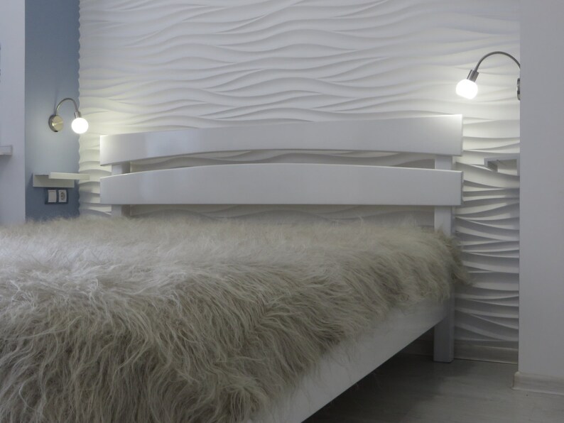 May include: A white bed frame with a fluffy white and gray blanket. The headboard is curved and has a modern design. The wall behind the bed is white with a textured pattern.