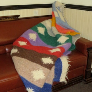 May include: A colorful striped blanket with white diamond patterns, draped over a brown leather couch.