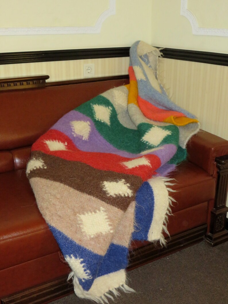 May include: A colorful striped blanket with white diamond patterns, draped over a brown leather couch.