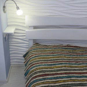 Puede incluir: Un marco de cama blanco con una manta a rayas. La pared detr&aacute;s de la cama tiene una textura ondulada.