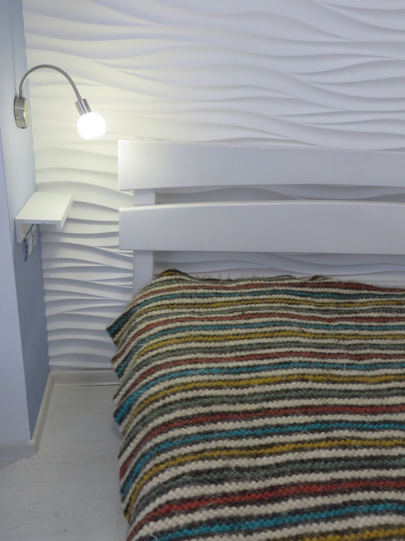 Puede incluir: Un marco de cama blanco con una manta a rayas. La pared detr&aacute;s de la cama tiene una textura ondulada.