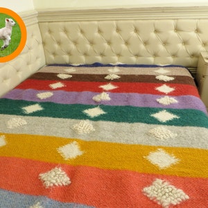 May include: A colorful striped throw blanket with white diamond-shaped patterns. The blanket is made of a soft, fuzzy material and has a rustic, handmade look.
