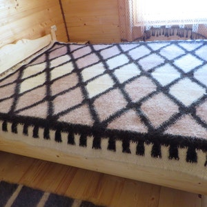 May include: A bed covered with a geometric patterned blanket. The blanket features a diamond pattern in shades of brown, cream, and black. The bed frame is made of light-colored wood. The room has wooden walls and flooring.