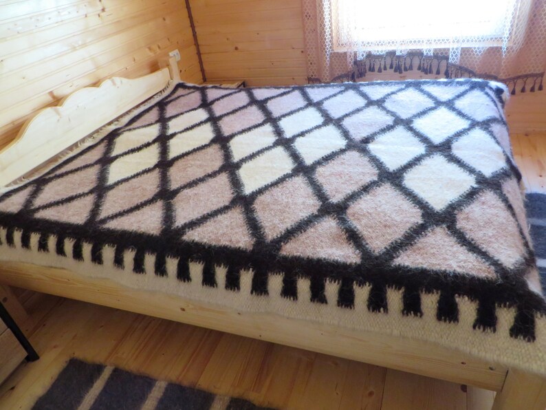 May include: A bed covered with a geometric patterned blanket. The blanket features a diamond pattern in shades of brown, cream, and black. The bed frame is made of light-colored wood. The room has wooden walls and flooring.