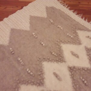 May include: A white and gray patterned rug with a geometric design. The rug has a soft, fuzzy texture.