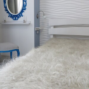 May include: A white fluffy bedspread with a white headboard and a blue chair in the background.