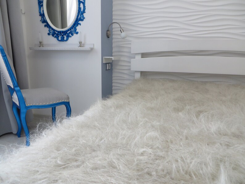 May include: A white fluffy bedspread with a white headboard and a blue chair in the background.