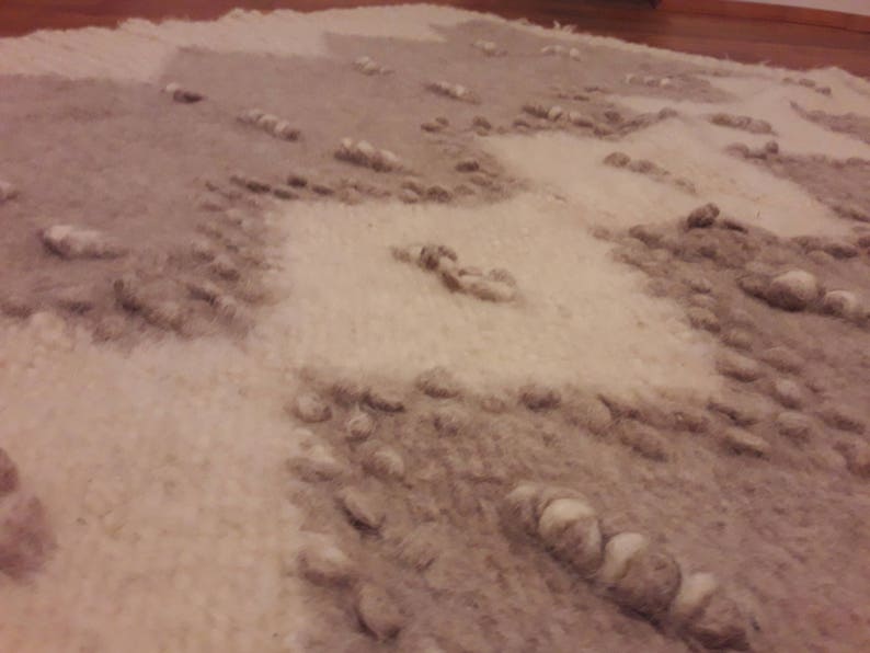 May include: A close-up of a white and beige rug with a textured, woven design. The rug has a subtle pattern of small, raised bumps.