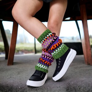 Könnte beinhalten: Ein Paar schwarze Canvas-Schuhe mit weißen Sohlen und bunten gestrickten Beinstulpen. Die Beinstulpen sind grün, orange, rosa, lila und weiß.