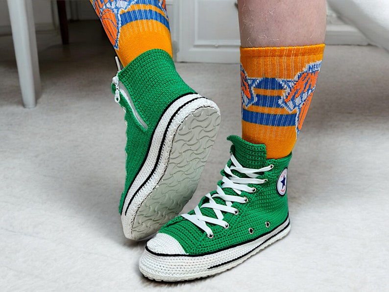 Puede incluir: Un par de zapatillas altas de crochet verde con cordones blancos y suela de goma blanca. Las zapatillas tienen un borde negro alrededor de la suela y un logotipo de estrella blanca en el lateral.