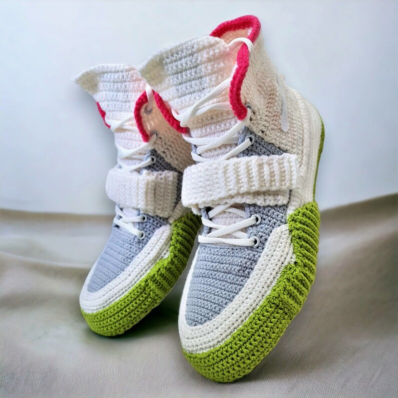 Pode incluir: Um par de t&ecirc;nis de croch&ecirc; com detalhes em branco, cinza e verde. Os t&ecirc;nis t&ecirc;m um design de cano alto e uma al&ccedil;a de velcro.