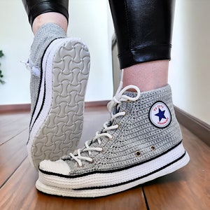May include: Gray crocheted high-top sneakers with white trim and a black star logo that says "Converse".