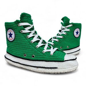 Puede incluir: Zapatillas altas de crochet verde con cordones blancos y suela blanca y negra. Las zapatillas tienen un logotipo de estrella azul con el texto "Converse" en el lateral.