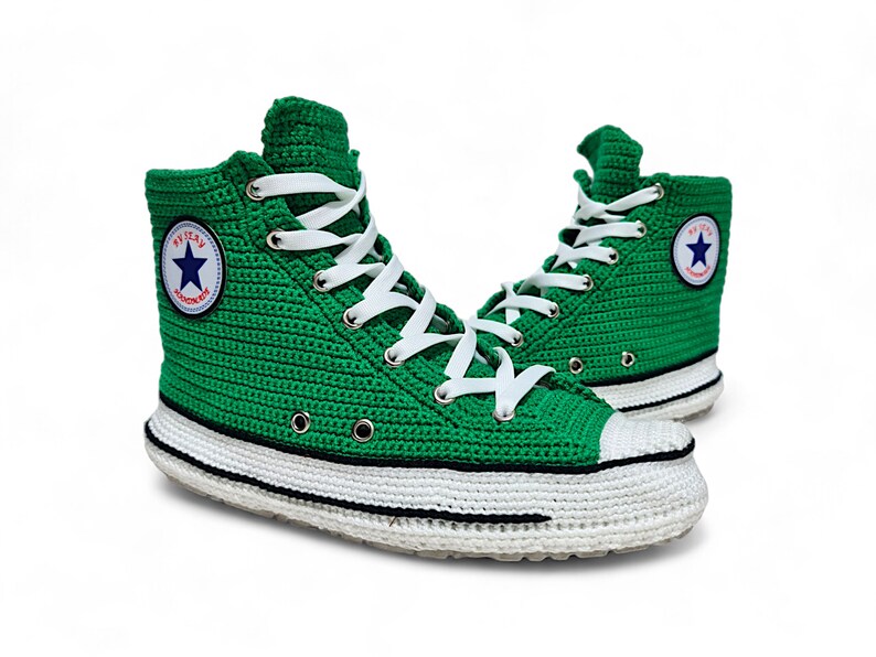 Puede incluir: Zapatillas altas de crochet verde con cordones blancos y suela blanca y negra. Las zapatillas tienen un logotipo de estrella azul con el texto "Converse" en el lateral.