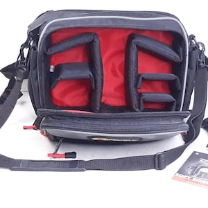May include: Black camera bag with red interior dividers and a gray zipper pull. The bag has an adjustable shoulder strap and a small pocket on the front. The bag has the text "30CT BOND SERIES ADVANCED CAMERA BAG" printed on the side.