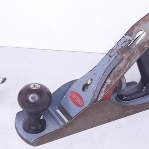 May include: A vintage Craftsman wood plane with a blue and brown body, a black handle, and a red and silver blade. The plane has a metal knob on the front.
