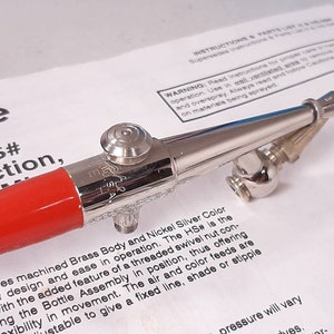 Peut inclure: Un a&eacute;rographe rouge et argent avec un &eacute;crou pivotant filet&eacute;. L'a&eacute;rographe a une poign&eacute;e rouge et un corps argent&eacute; avec une couleur argent nickel. Le texte "HS#" est visible sur l'a&eacute;rographe.