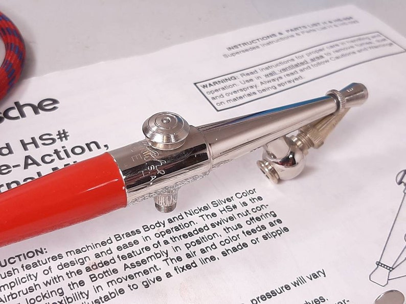 Peut inclure: Un a&eacute;rographe rouge et argent avec un &eacute;crou pivotant filet&eacute;. L'a&eacute;rographe a une poign&eacute;e rouge et un corps argent&eacute; avec une couleur argent nickel. Le texte "HS#" est visible sur l'a&eacute;rographe.