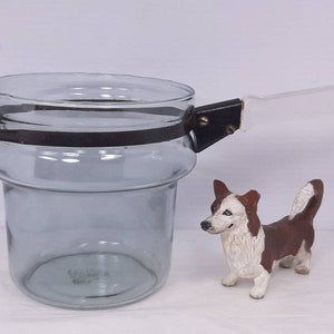 May include: A clear glass jar with a black metal band around the top and a clear plastic handle. The jar is sitting on a white surface.