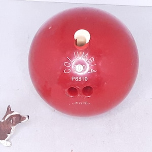 May include: A red bowling ball with white lettering that says "Columbia" and "P6310".