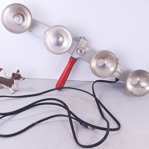 May include: A silver metal hand-held bell ringer with four bells and a red handle. The bell ringer is connected to a black electrical cord.