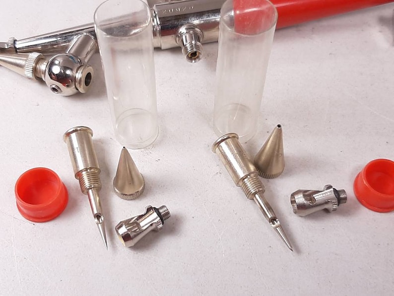 Peut inclure: Un ensemble d'outils d'a&eacute;rographe, comprenant un a&eacute;rographe argent&eacute;, deux tubes en plastique transparent, deux aiguilles argent&eacute;es, deux embouts argent&eacute;s, une buse argent&eacute;e et deux bouchons rouges.