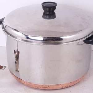 May include: A stainless steel pot with a copper bottom and a black lid. The pot has two black handles.
