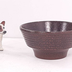 May include: A brown ceramic bowl with a textured, speckled finish. The bowl has a wide, rounded base and a flared lip.