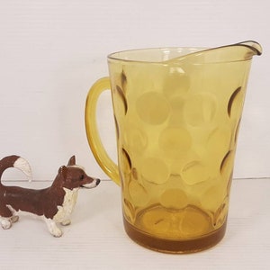 May include: A yellow glass pitcher with a textured, bubble-like design. The pitcher has a handle and a wide mouth.