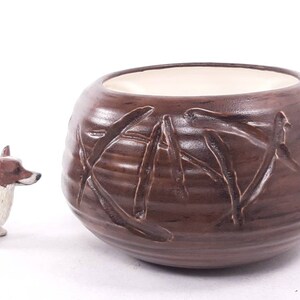 May include: A brown ceramic planter with a textured bamboo design. The planter has a white glazed interior.