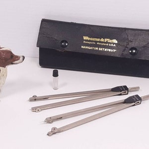 May include: A black leather case with the words "Weems & Plath Annapolis, Maryland U.S.A. NAVIGATOR SET #761/7" printed on it. The case contains a set of three silver compasses and a small clear glass vial.