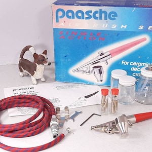 Peut inclure: Ensemble d'a&eacute;rographe Paasche &agrave; simple action avec un tuyau d'air rouge et bleu, deux petits flacons avec des bouchons rouges, trois bocaux en verre et un a&eacute;rographe avec une poign&eacute;e rouge.