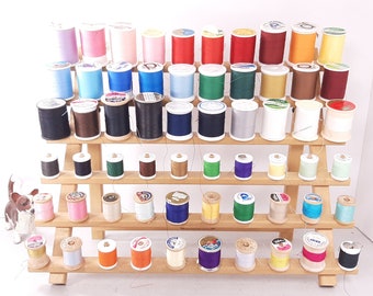 May include: A wooden thread rack with four tiers holds a variety of spools of thread in different colors, including black, white, brown, blue, green, red, orange, and pink.