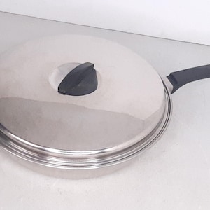 May include: Stainless steel frying pan with a lid and a black handle. The lid has a black handle and a vent hole. The pan is round and has a shiny, reflective surface. A kitchenware item.