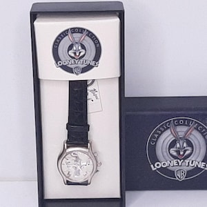 May include: A Looney Tunes Classic Collection wristwatch in its original box. The watch has a silver-tone case, a black leather band, and a Bugs Bunny design on the face. The box features the Looney Tunes logo.