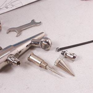 Peut inclure: Un kit d'a&eacute;rographe argent&eacute; avec divers accessoires, dont une cl&eacute;, une buse et une aiguille. Le kit comprend &eacute;galement un support pour l'a&eacute;rographe.