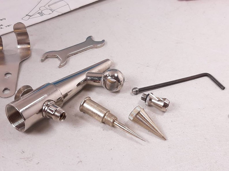 Peut inclure: Un kit d'a&eacute;rographe argent&eacute; avec divers accessoires, dont une cl&eacute;, une buse et une aiguille. Le kit comprend &eacute;galement un support pour l'a&eacute;rographe.