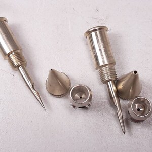 Peut inclure: Un ensemble de cinq buses d'a&eacute;rographe en m&eacute;tal argent&eacute;. Les buses sont de tailles et de formes diff&eacute;rentes, certaines ayant une pointe pointue et d'autres une pointe ronde.