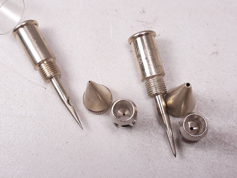 Peut inclure: Un ensemble de cinq buses d'a&eacute;rographe en m&eacute;tal argent&eacute;. Les buses sont de tailles et de formes diff&eacute;rentes, certaines ayant une pointe pointue et d'autres une pointe ronde.