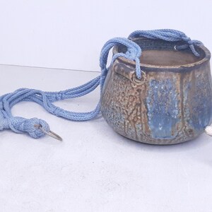 May include: A blue ceramic hanging planter with a light blue rope. The planter has a mottled brown and blue glaze.