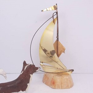 May include: A gold sailboat sculpture on a beige stone base. The sailboat has a small flag and is made of wire and metal.