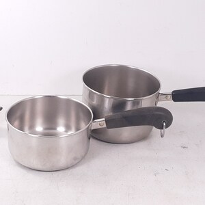 May include: Two stainless steel saucepans with black handles. The smaller saucepan is on the left and the larger saucepan is on the right. Both saucepans have a shiny finish.