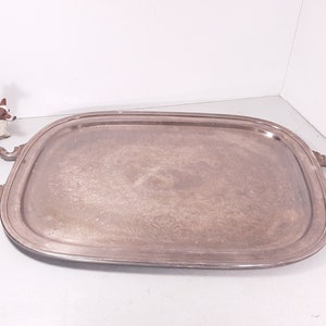 May include: Silver-toned rectangular serving tray with ornate handles. The tray has a slightly raised edge and a decorative floral pattern on the surface. A small ceramic dog figurine is in the background.