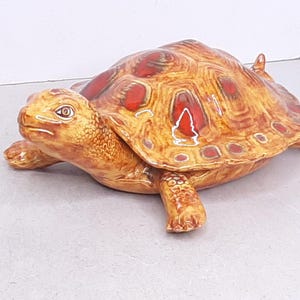 May include: A ceramic turtle figurine with a detailed shell pattern in shades of brown and red. The turtle has a detailed head and legs, and is a decorative item.