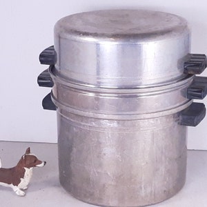 May include: A silver three-tiered steamer with black handles. The steamer is made of metal and has a shiny finish.