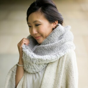 May include: A woman wearing a white cardigan with a gray and white faux fur scarf. The cardigan has a textured knit pattern.